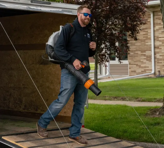 WPM maintenance worker walking out of a WPM trailer holding a leaf blower